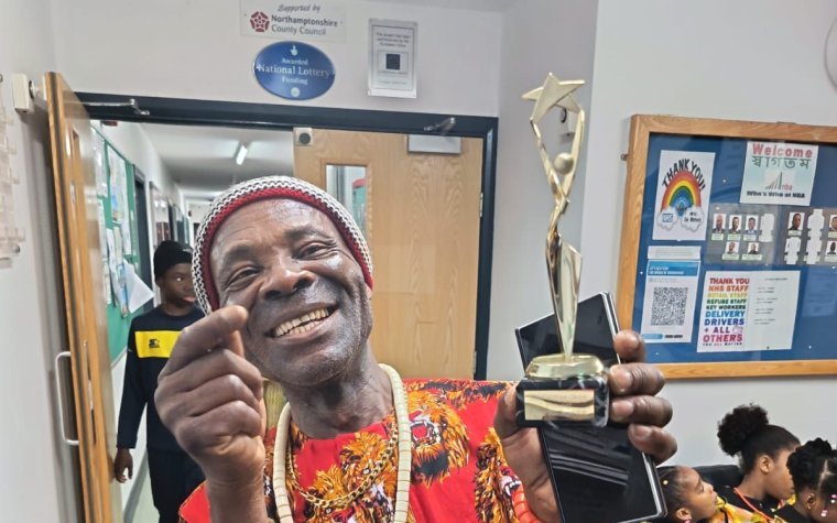 Igbo Union Northamptonshire - A smiling member in a red cap and patterned shirt holding an award