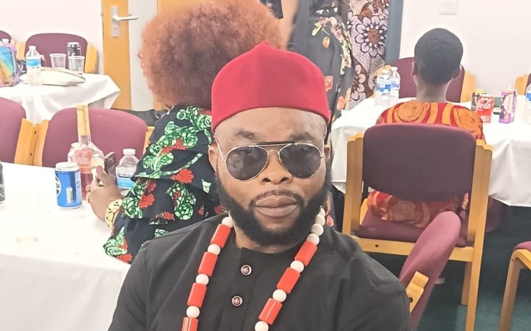 Igbo Union Northamptonshire - A member in a red cap and coral beads seated with a carved staff