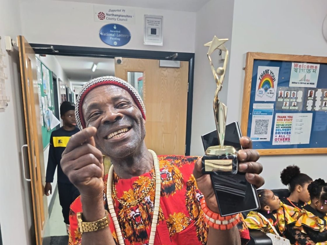 Igbo Union Northamptonshire - A smiling member in a red cap and patterned shirt holding an award